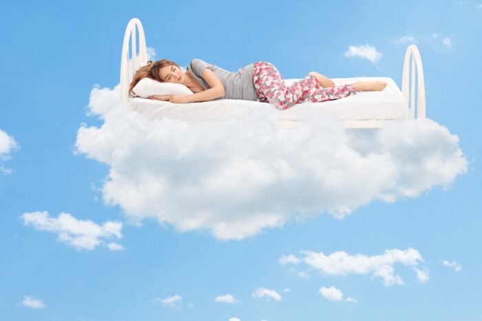 woman asleep on bes floting in the clouds
