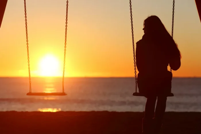 Woman sitting next to an empty swing